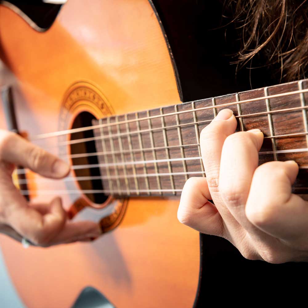 Close-up of a learner playing an acoustic guitar.