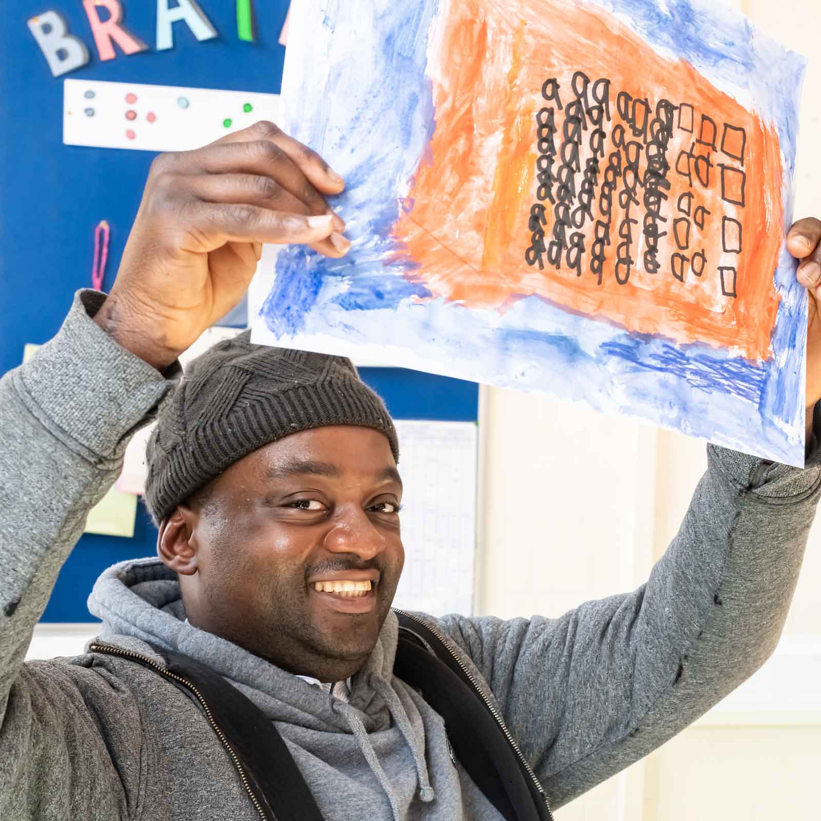 Learner smiling and holding up a colourful painting created in a Supported Learning art session.