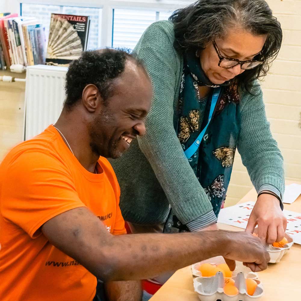 Tutor supporting a learner with a hands-on activity at a table.