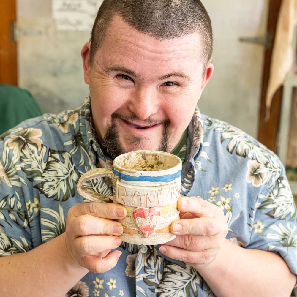Learner smiling and holding a handmade ceramic mug.