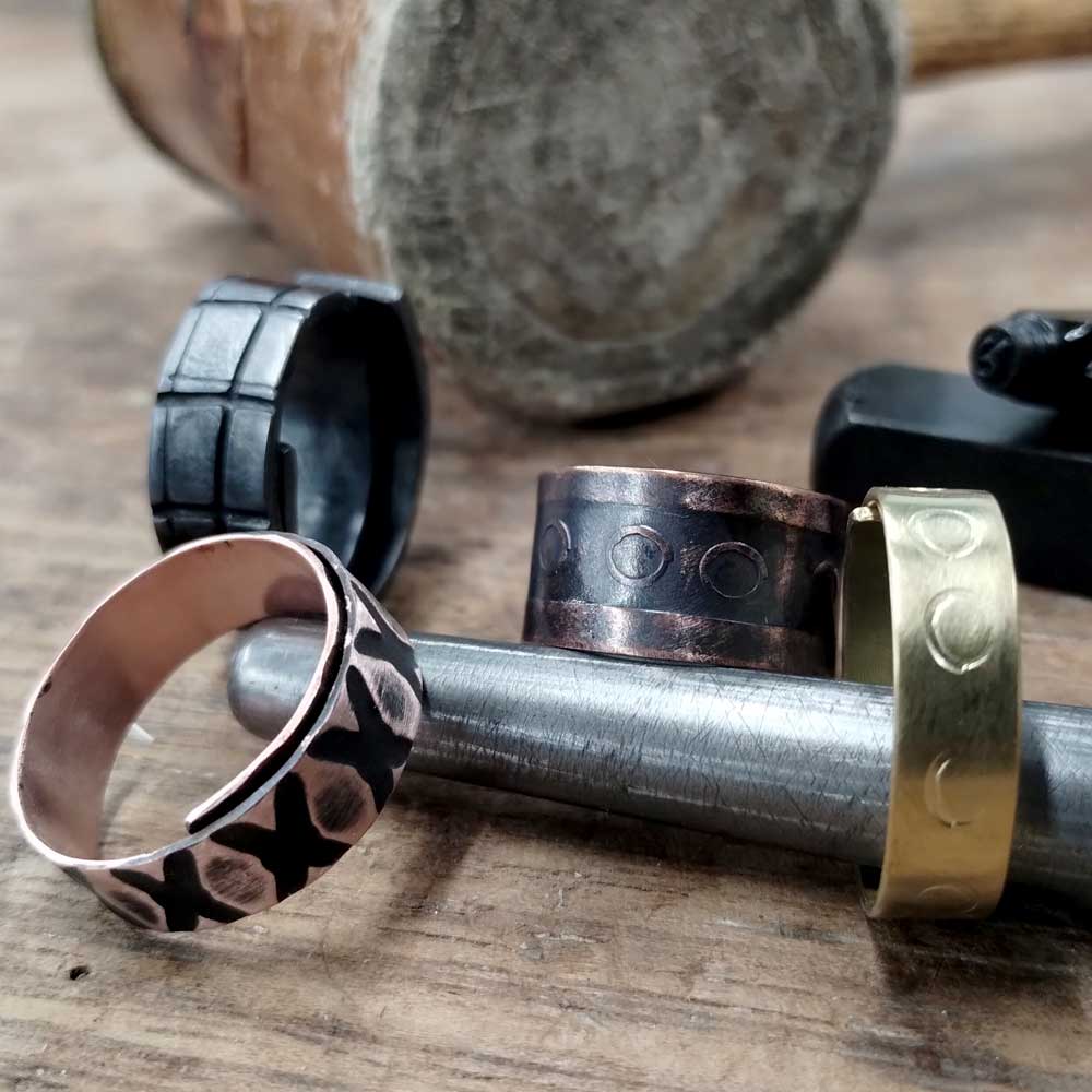 Handmade stamped copper and brass rings on a ring mandrel